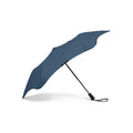 The Blunt Mini Metro Umbrella in blue features a compact, asymmetrical canopy and a black handle with wrist strap, displayed on a white background.