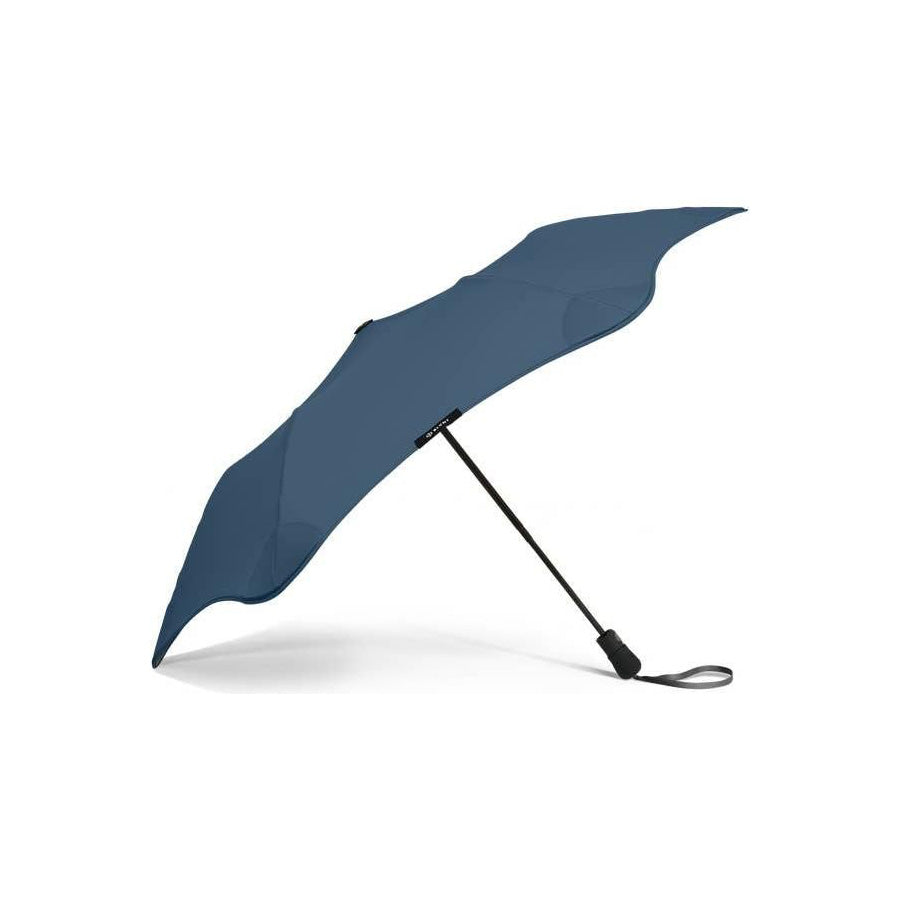 The Blunt Mini Metro Umbrella in blue features a compact, asymmetrical canopy and a black handle with wrist strap, displayed on a white background.