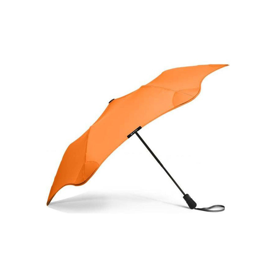 The Blunt Mini Metro Umbrella, in orange, features a black handle and wrist strap. It is shown open against a plain white background.