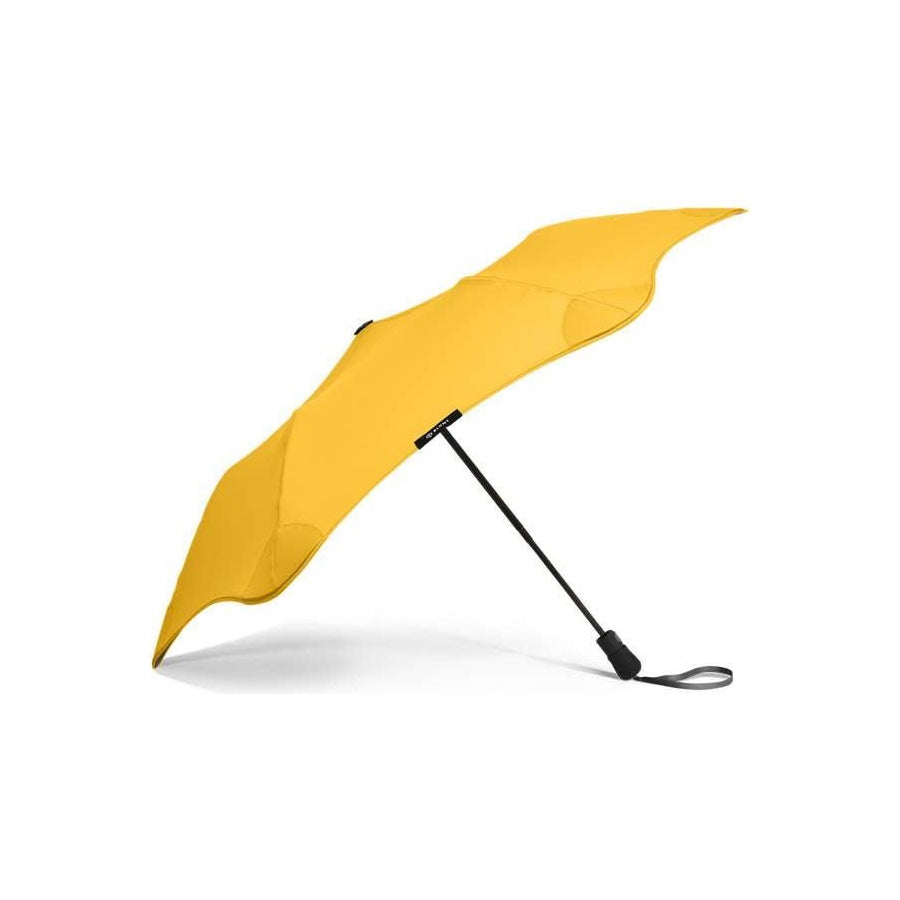 The Blunt Mini Metro Umbrella features a yellow, curved, asymmetrical canopy and a black handle, displayed against a plain white background.