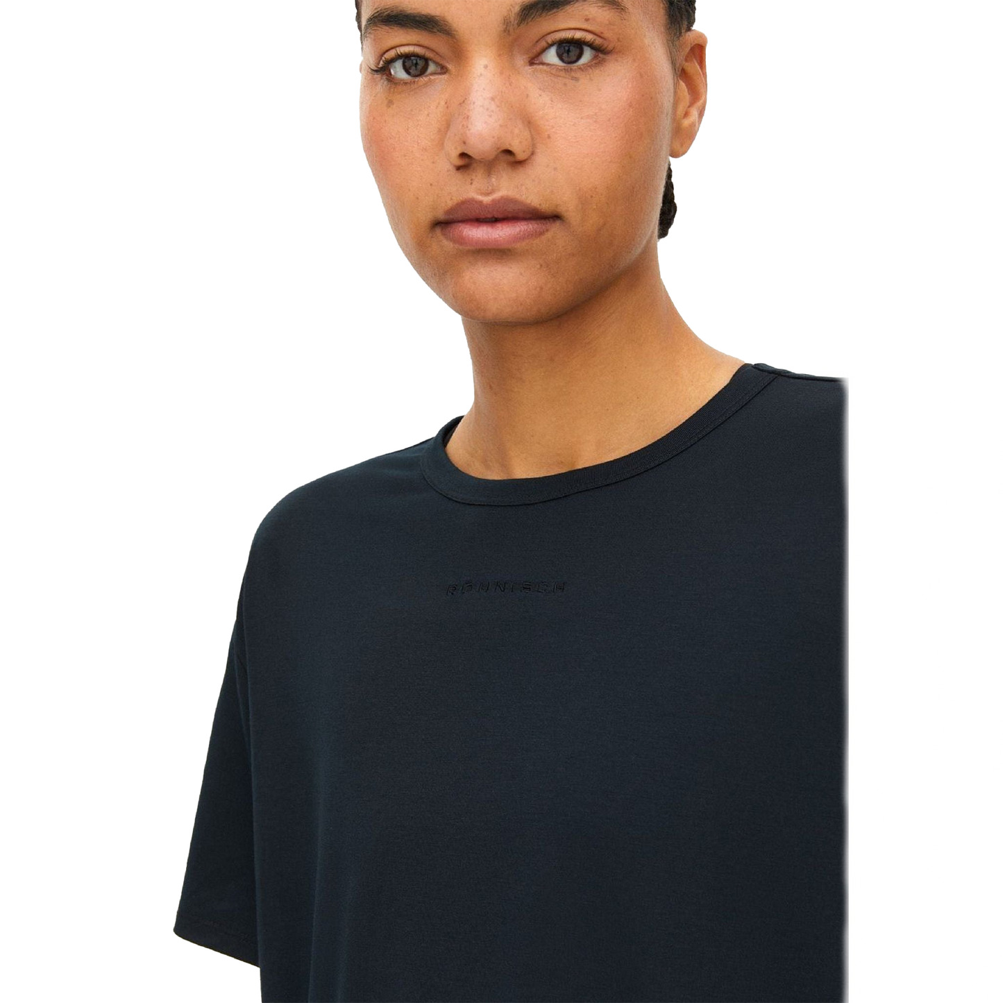 A person with short hair is wearing the Clara Base Tee by Rohnisch, a plain black T-shirt made from recycled polyester, featuring subtle text on the chest against a black background.