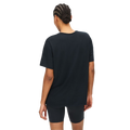 A person, seen from behind against a plain backdrop, wears Rohnisch's Clara Base Tee—a loose silhouette black t-shirt made from recycled polyester—and black shorts.