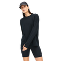 A person in a Rohnisch Clara Base LS shirt made from recycled polyester, paired with black shorts and a cap, stands against a white backdrop.