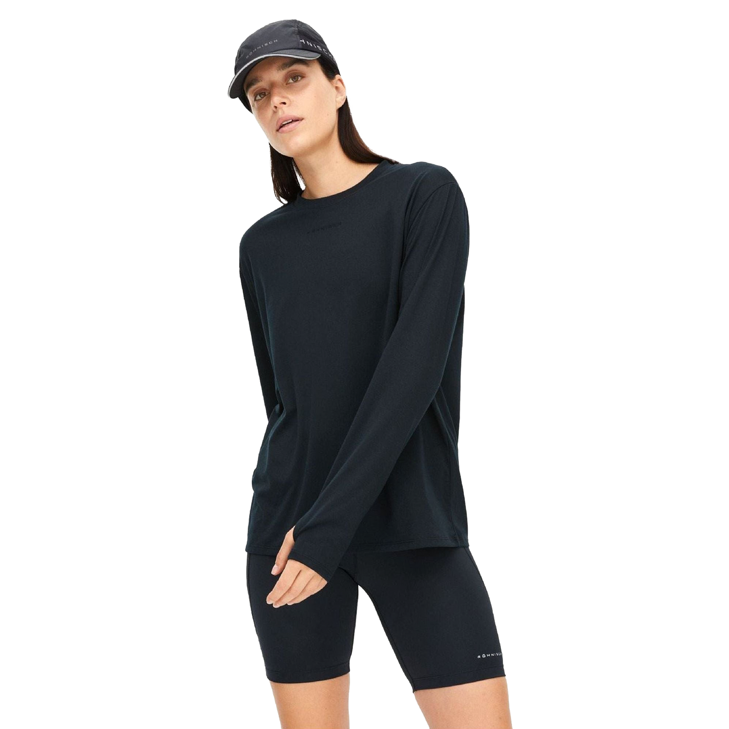 A person in a Rohnisch Clara Base LS shirt made from recycled polyester, paired with black shorts and a cap, stands against a white backdrop.