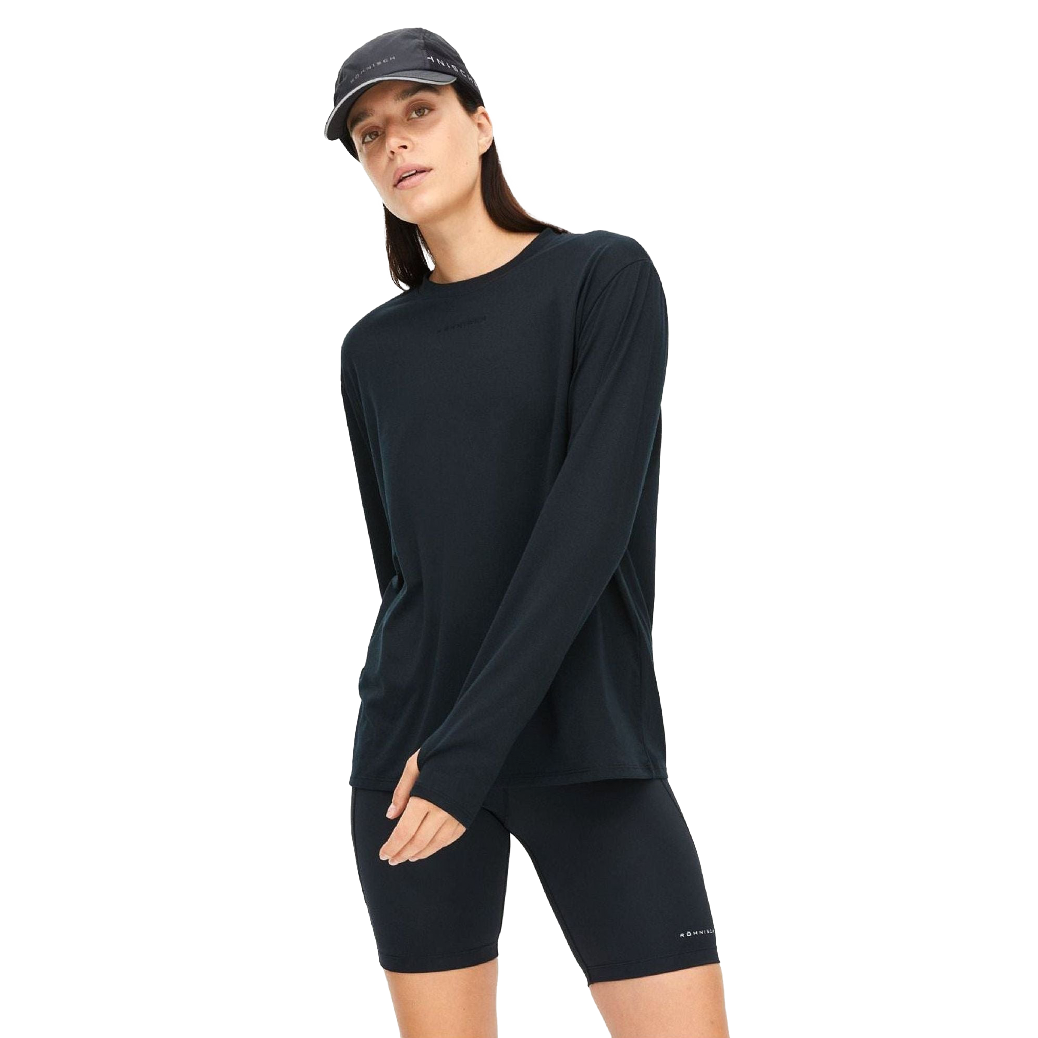 A person in a Rohnisch Clara Base LS shirt made from recycled polyester, paired with black shorts and a cap, stands against a white backdrop.