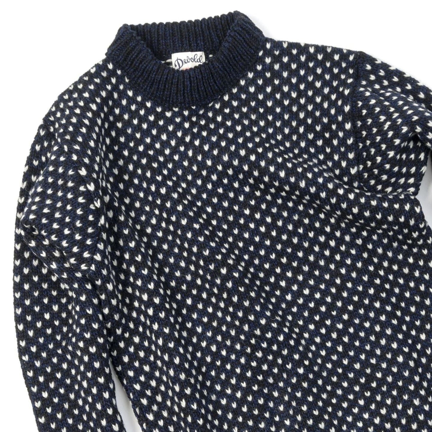 The Nordsjo Crew Neck by Devold is a navy and white patterned knit sweater made of Norwegian wool. It features a ribbed collar, small teardrop designs, and offers unisex fit versatility with a text label inside.