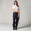 A person stands against a plain background, wearing a white t-shirt, black shoes, and Seven Gauge's blu Trouser Tropical Wool with hands clasped in front; the classic tailoring exudes elegance and sophistication.