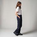 A person stands sideways with hands in pockets, wearing a white t-shirt and classic black Seven Gauge "Trouser Tropical Wool, Blu" pants paired with black shoes against a plain background.