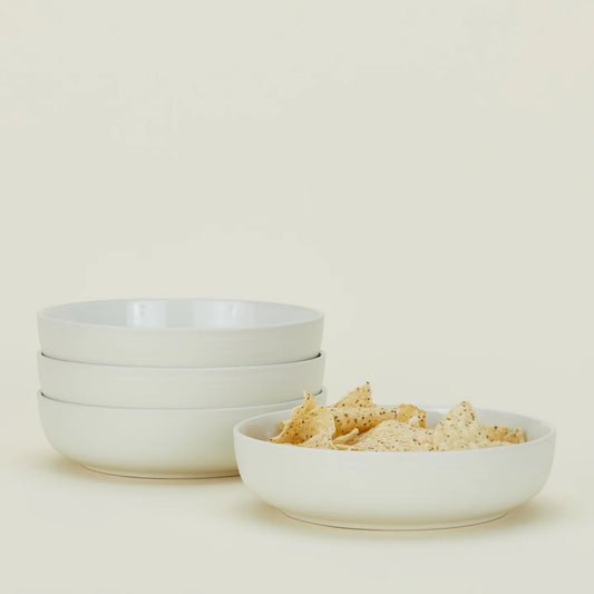 A stack of three empty white Hawkins New York Essential Low Bowls (Set of 4) sits next to a matching bowl filled with tortilla chips against a plain light background.
