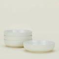 Four Essential Low Bowls by Hawkins New York are stacked on the left, with one set apart on the right against a light background. Each stoneware bowl is microwave and dishwasher safe for everyday convenience. Set includes 4 bowls.