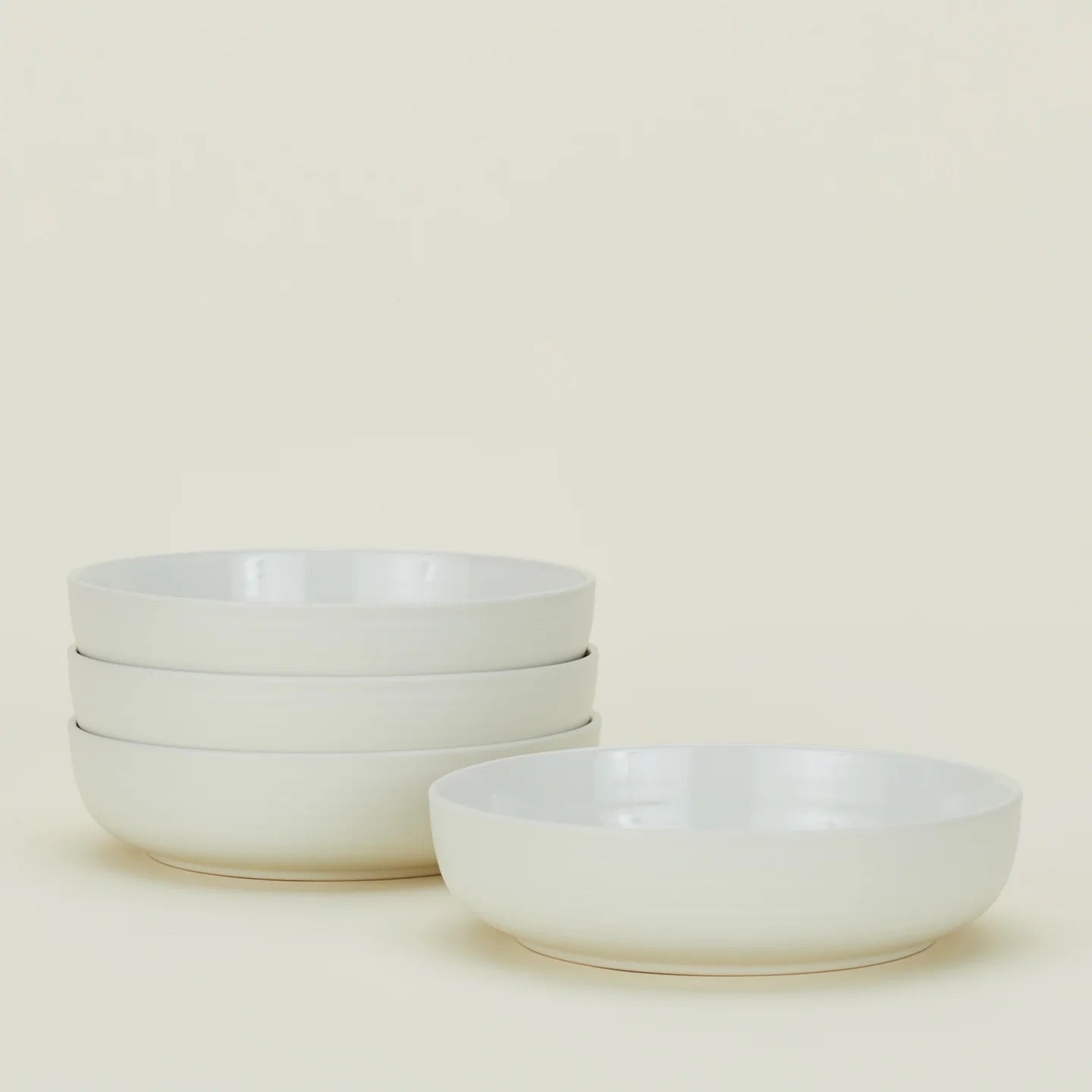 Four Essential Low Bowls by Hawkins New York are stacked on the left, with one set apart on the right against a light background. Each stoneware bowl is microwave and dishwasher safe for everyday convenience. Set includes 4 bowls.