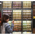A child in a denim jacket examines a jar of Edmund Fallot Dijon Mustards from Gourmet Food Solutions, Inc. in front of a display filled with jars of various preserves on shelves.