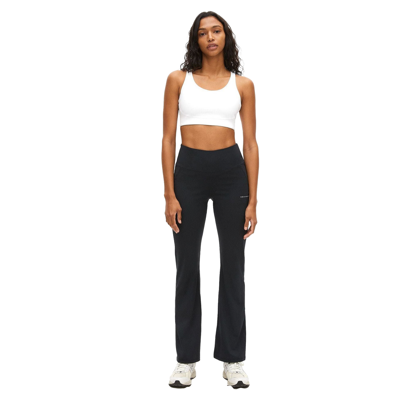 Facing forward, a woman wears Rohnisch's Flattering High Waist Pants and a white sports bra made from breathable fabric. Her look is completed with white sneakers against the plain background.