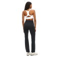 A person is standing against a white background, facing away, wearing a white sports bra, Rohnisch Flattering High Waist Pants made with breathable fabric in black, and white sneakers.