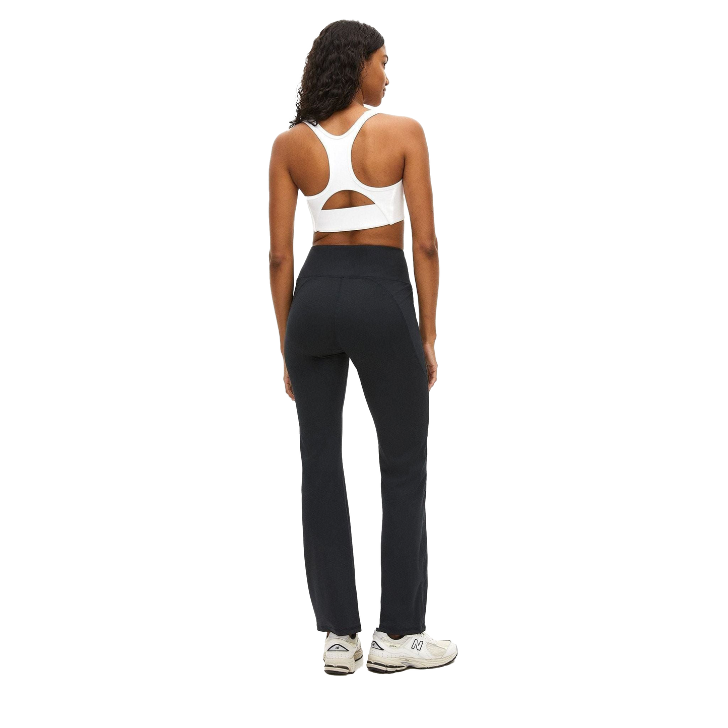 A person is standing against a white background, facing away, wearing a white sports bra, Rohnisch Flattering High Waist Pants made with breathable fabric in black, and white sneakers.