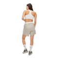 A person faces away, wearing a white sports bra and beige Frankie Wind Shorts by Rohnisch, featuring the logo. They pair them with white socks and gray sneakers.