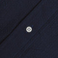 Close-up of the Gitman Vintage Overdye Seersucker Shirt in navy, showing its textured fabric and a white four-hole button sewn along a diagonal seam.