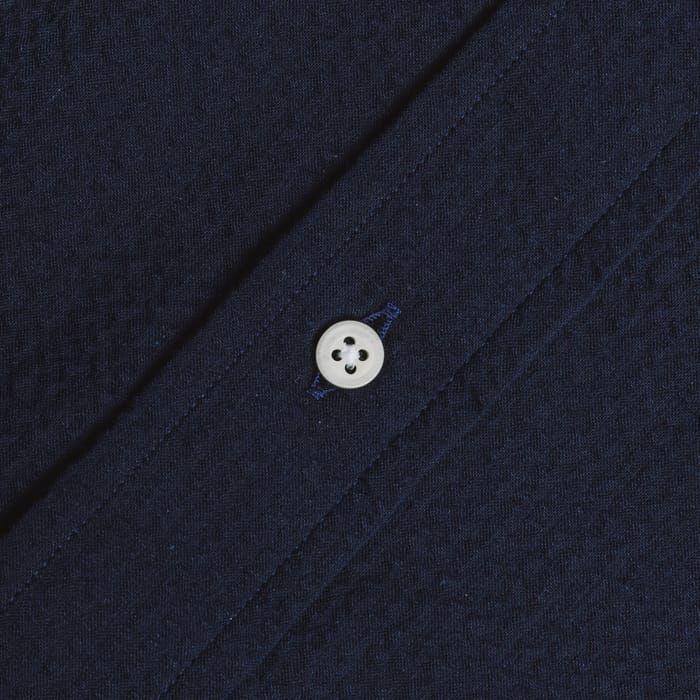 Close-up of the Gitman Vintage Overdye Seersucker Shirt in navy, showing its textured fabric and a white four-hole button sewn along a diagonal seam.