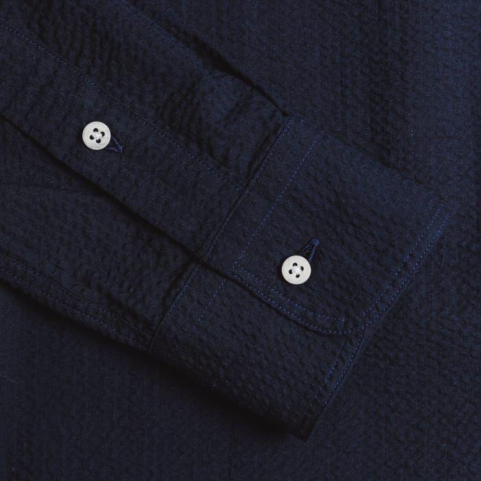 Close-up of the Gitman Vintage Overdye Seersucker Shirt in Navy, featuring a textured dark blue sleeve with two white buttons and visible stitching.