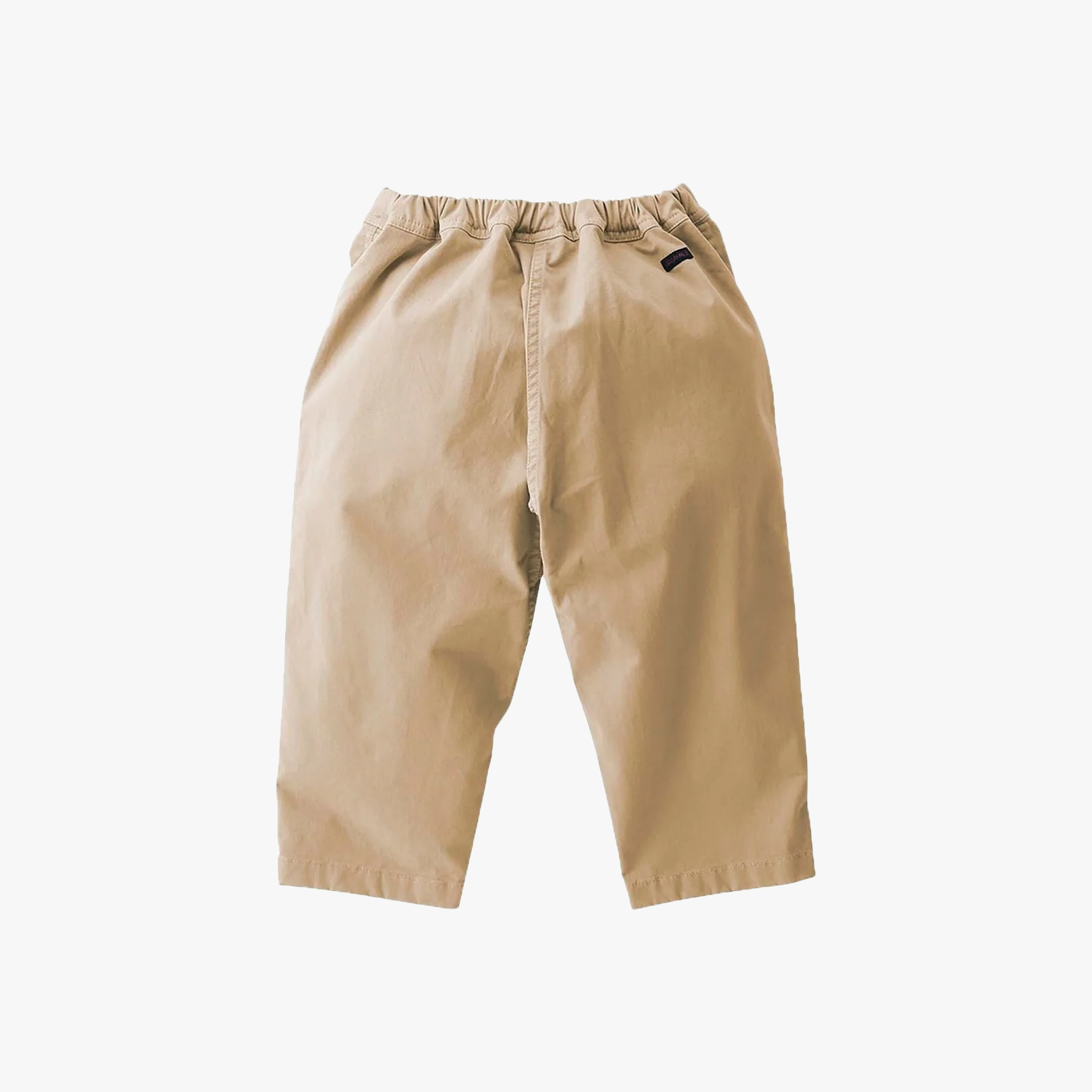The Gramicci K Loose Tapered Pant, Chino is a pair of beige kids' cropped outdoor pants made from stretch twill with an elastic waistband and a small black tag near the pocket, shown on a white background.