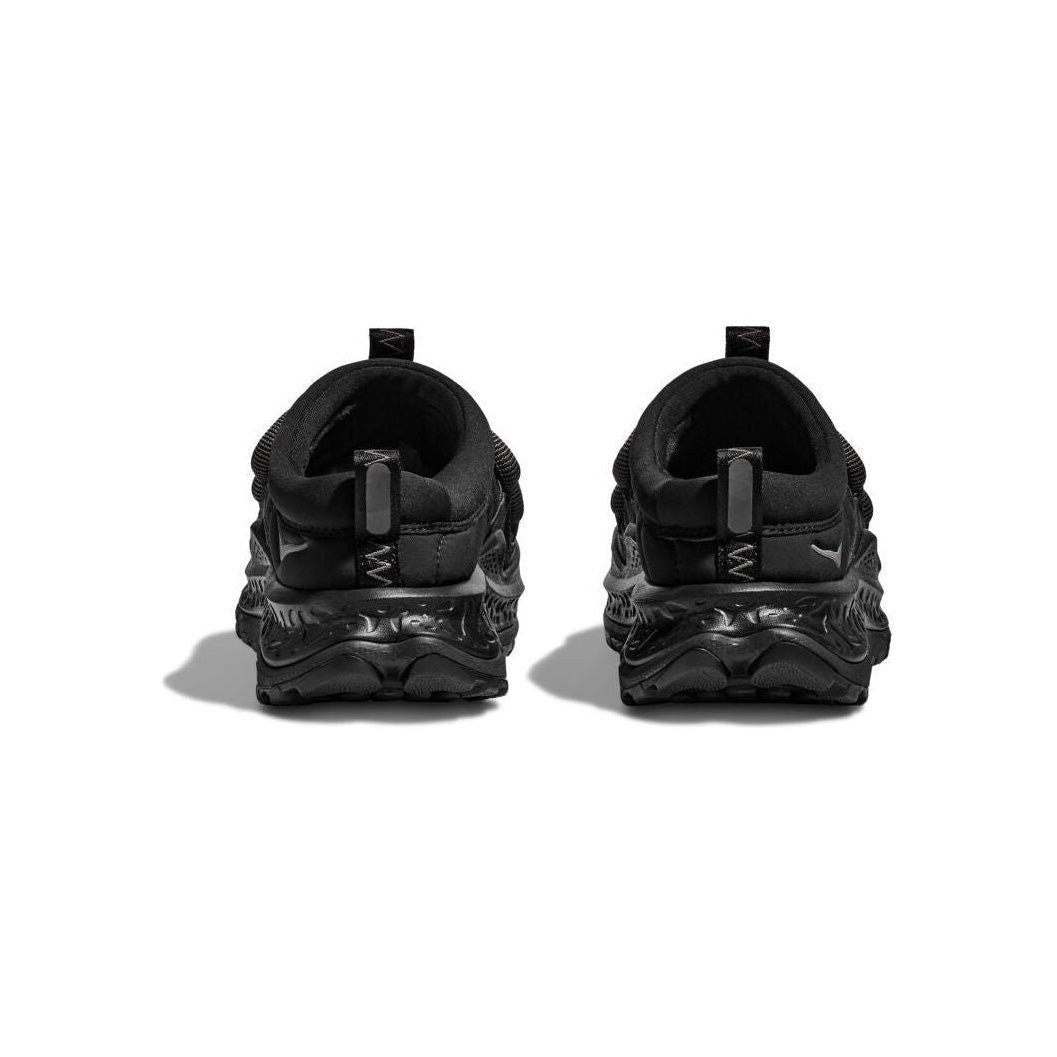 Back view of Hoka's U Ora Primo in black, featuring glossy, patterned soles and a slip-on comfort design against a white background.