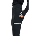 A person wearing black Rohnisch Insulate Wind Shield Tights with an elastic drawstring and a black top stands against a plain background.
