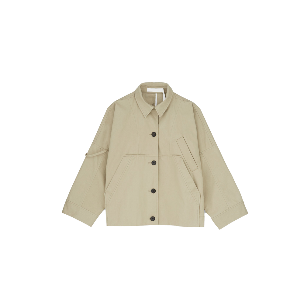 The Aiayu Jules Jacket is a beige, long-sleeve, oversized button-up with large front pockets and a collar. It's made from weather-resistant Ventile fabric, combining style and practicality against a white background.