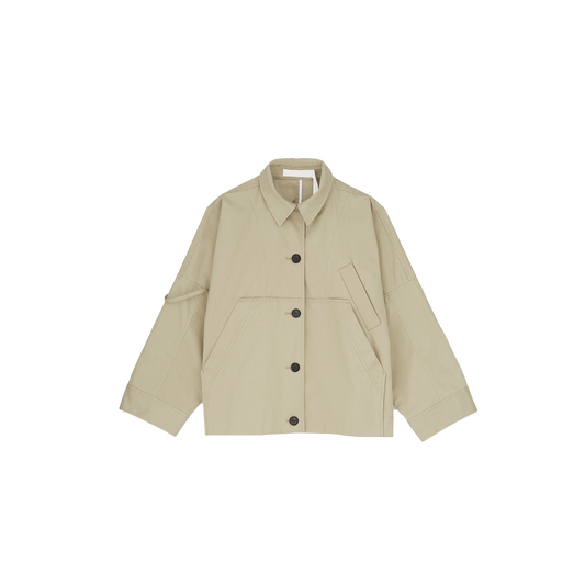 The Aiayu Jules Jacket is a beige, long-sleeve, oversized button-up with large front pockets and a collar. It's made from weather-resistant Ventile fabric, combining style and practicality against a white background.