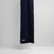 The Le Bonnet "Midnight" scarf, featuring a long, dark blue lambswool design and a small white label, is set against a plain gray background.
