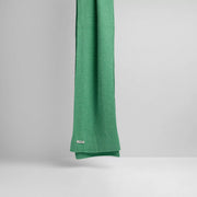 The Jade scarf from Le Bonnet drapes elegantly against a light gray backdrop, adding a refined touch to the scene.