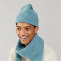 A person wearing a Basil beanie and matching scarf by Le Bonnet, smiling warmly in a neutral setting.