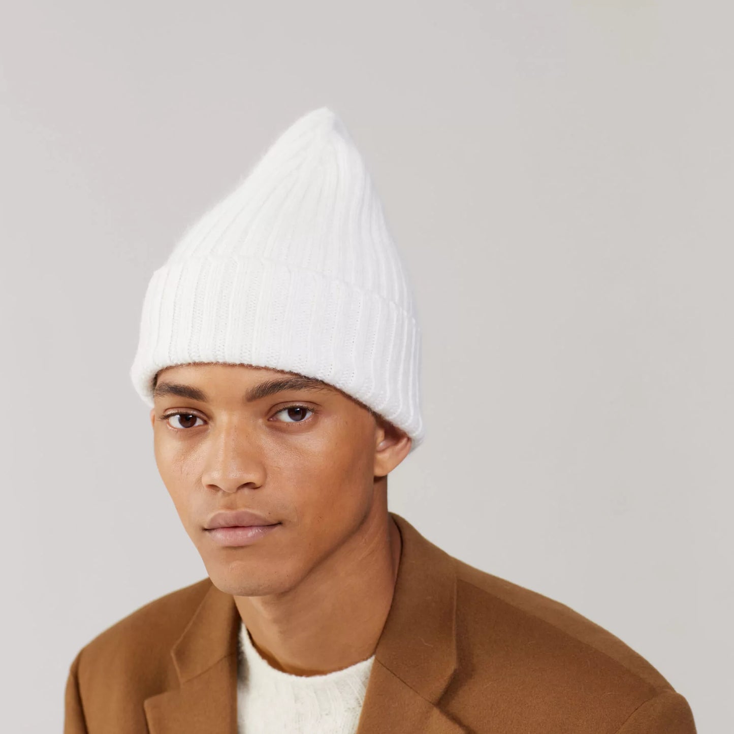 Wearing a Large Beanie in Snow by Le Bonnet, the person complements it with a brown coat against a plain background.
