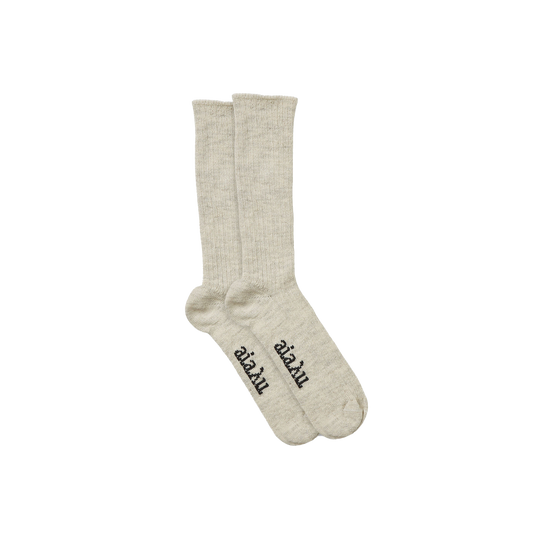 The Aiayu Llama Socks are a beige, unisex pair made from thermoregulating llama wool, featuring black text on the soles over a black background.