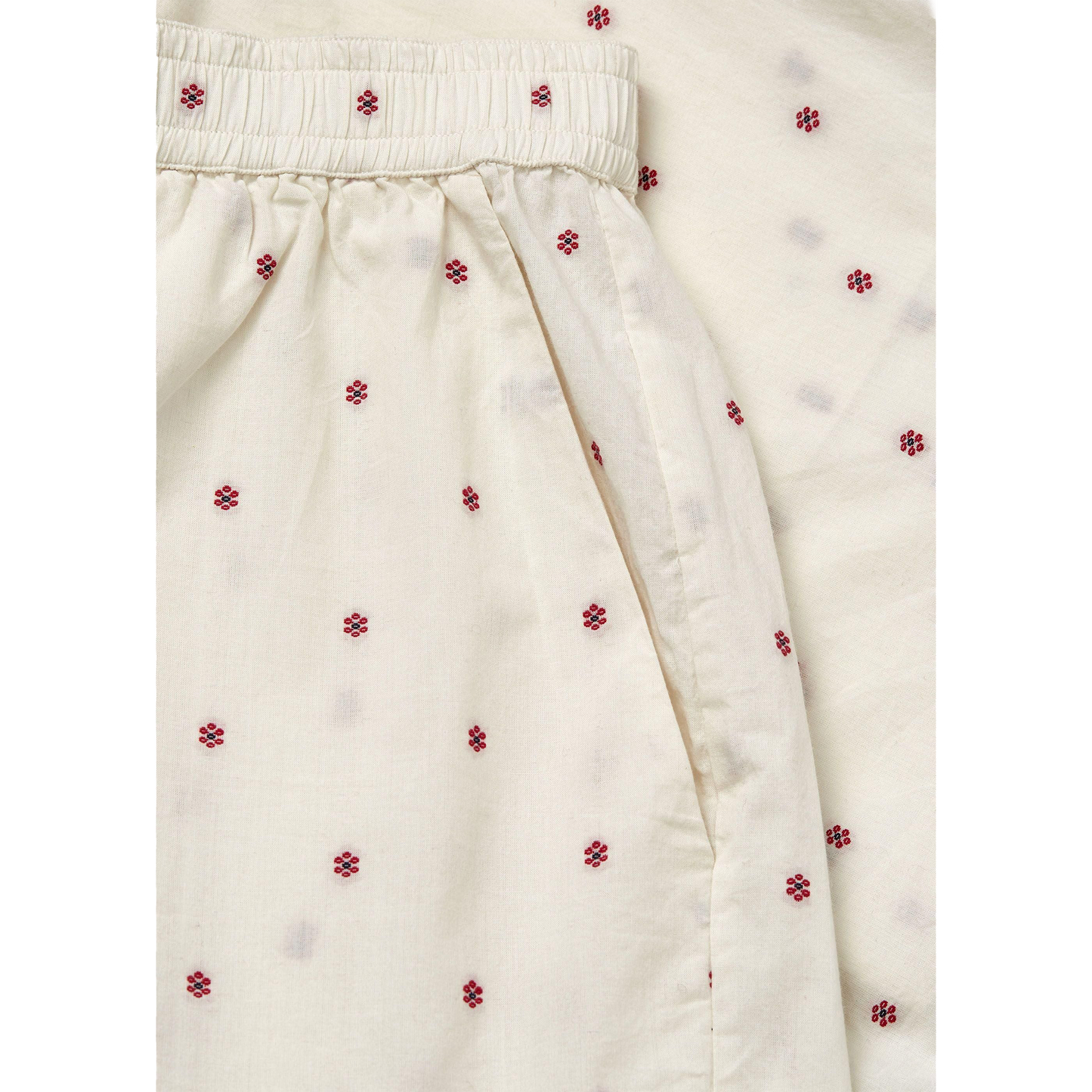 Close-up of cream-colored fabric with small red flower patterns, gathered at the top with an elastic waistband, resembling Aiayu's Lulu Shorts Flore in Mix Creme made from regenerative cotton.