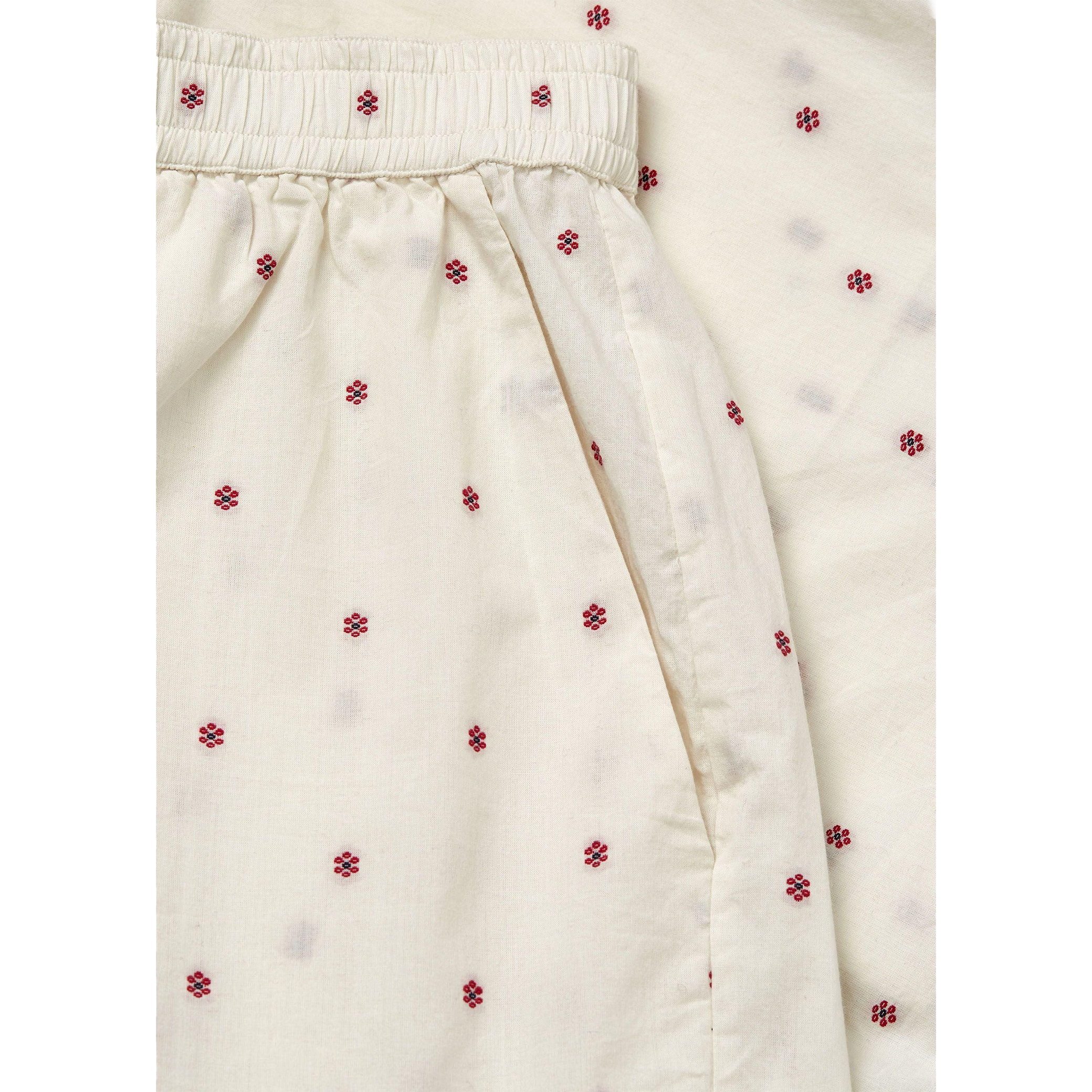 Close-up of cream-colored fabric with small red flower patterns, gathered at the top with an elastic waistband, resembling Aiayu's Lulu Shorts Flore in Mix Creme made from regenerative cotton.