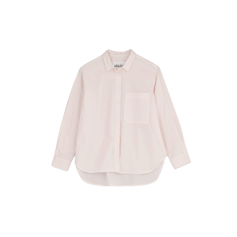 The Lynette Shirt by Aiayu is a light pink, oversized button-up with long sleeves and a front pocket, crafted from organic cotton against a plain backdrop. Embrace sustainable fashion with this stylish piece.