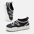 The Park Icon slip-on sneakers by Moon Boot are black and white with ultra-flexible construction. They feature white soles, handy heel loops, and brand text on the tongue and side.