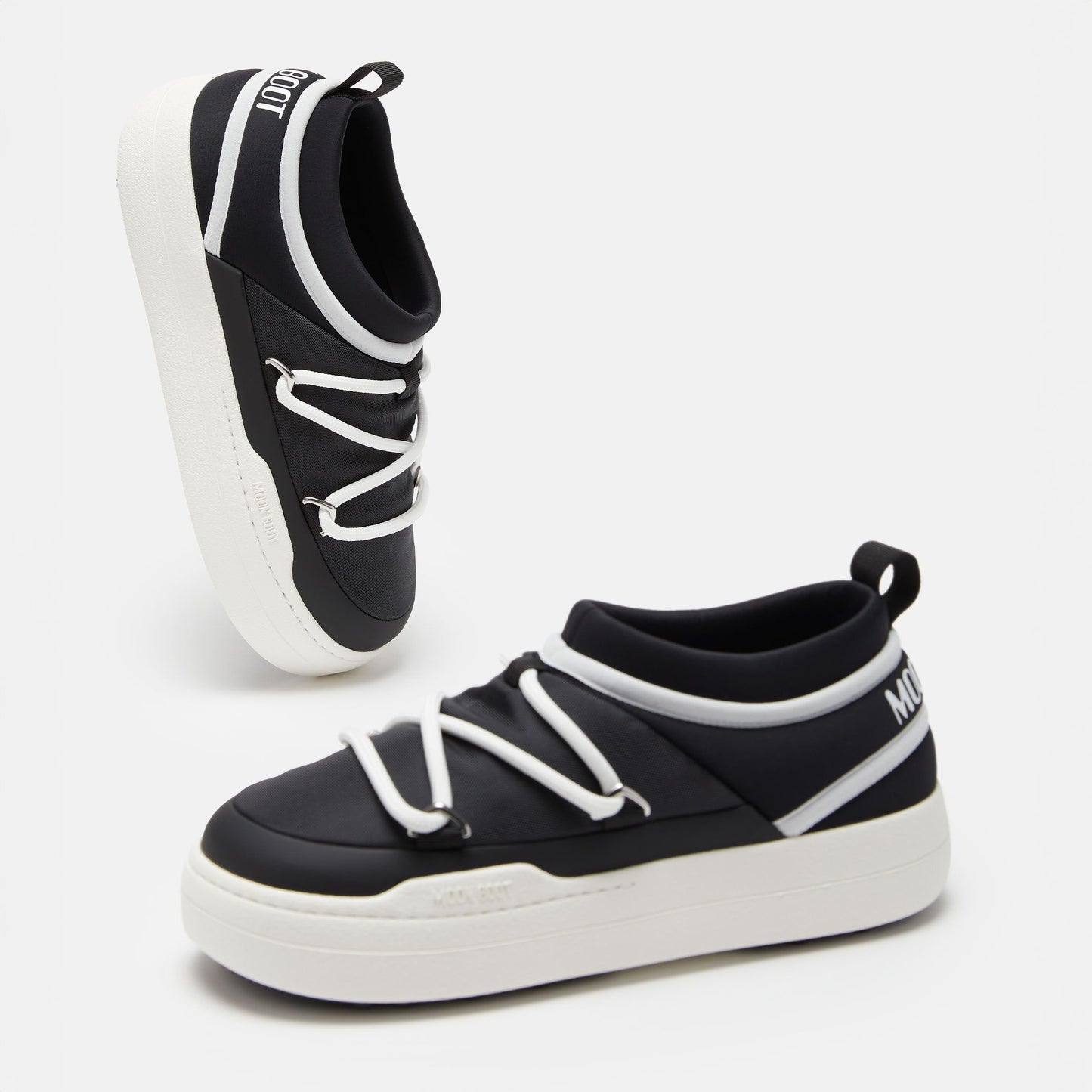 The Park Icon slip-on sneakers by Moon Boot are black and white with ultra-flexible construction. They feature white soles, handy heel loops, and brand text on the tongue and side.