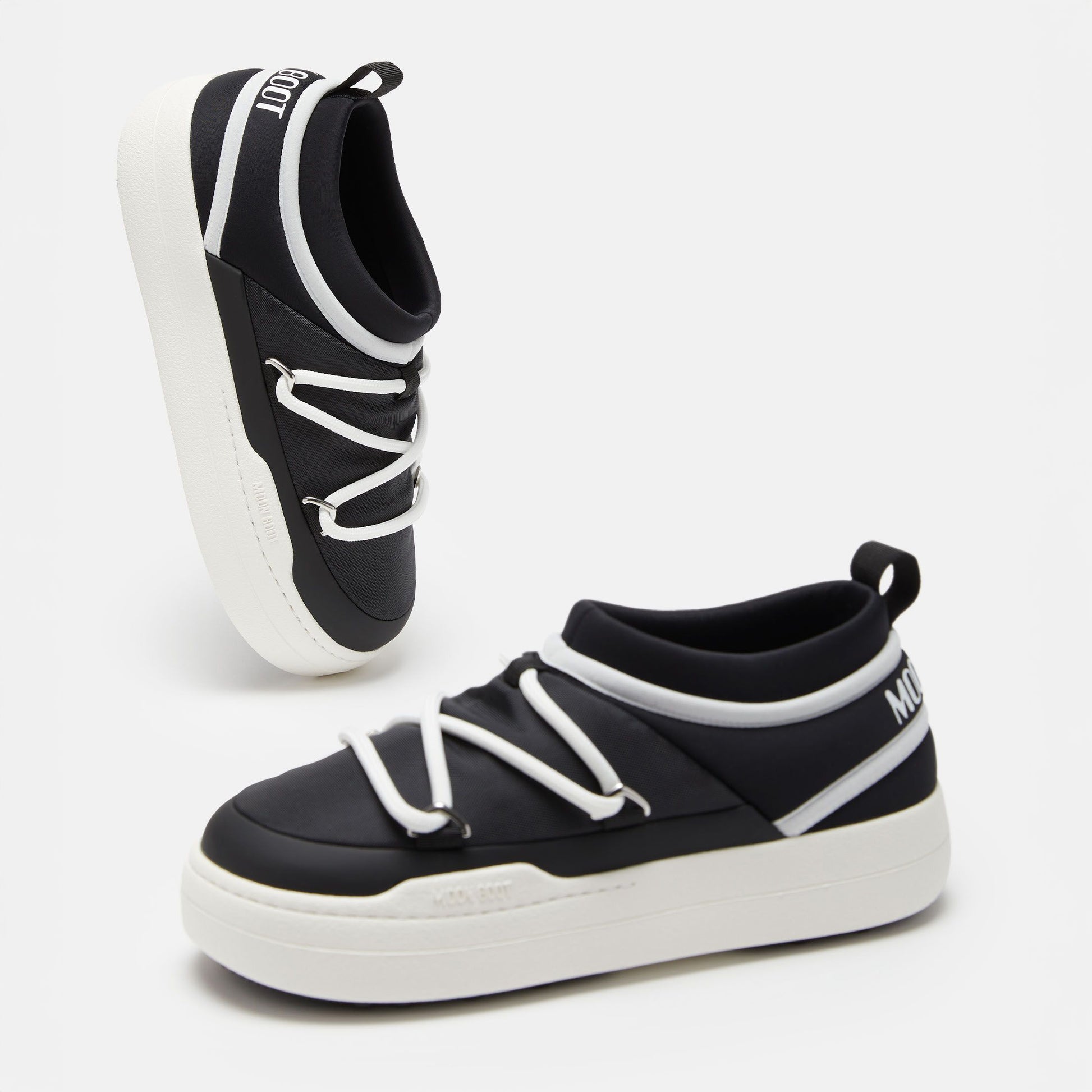 The Park Icon slip-on sneakers by Moon Boot are black and white with ultra-flexible construction. They feature white soles, handy heel loops, and brand text on the tongue and side.