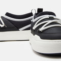 Close-up of Moon Boot's Park Icon sneakers, black and white with ultra-flexible construction, featuring thick white soles and intertwined laces set against a plain white background.