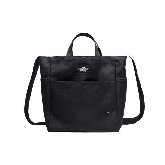The Multi Pocket Bag Medium by Bags in Progress is a medium-sized black tote crafted from water-repellent nylon canvas, featuring two handles, a shoulder strap for versatile carrying, and a convenient front pocket.