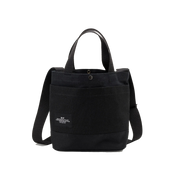 The New York Tote Small by Bags in Progress is a black cotton canvas tote bag featuring dual handles, an adjustable shoulder strap, and a front pocket with a small label on the front.