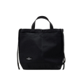 The Bags in Progress New York Tote Medium is a black rectangular cotton canvas bag made in Japan, featuring short handles, an adjustable shoulder strap, and a small white label at the bottom front center.