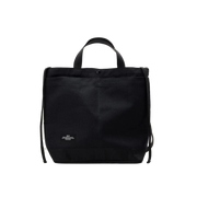 The Bags in Progress New York Tote Medium is a black rectangular cotton canvas bag made in Japan, featuring short handles, an adjustable shoulder strap, and a small white label at the bottom front center.
