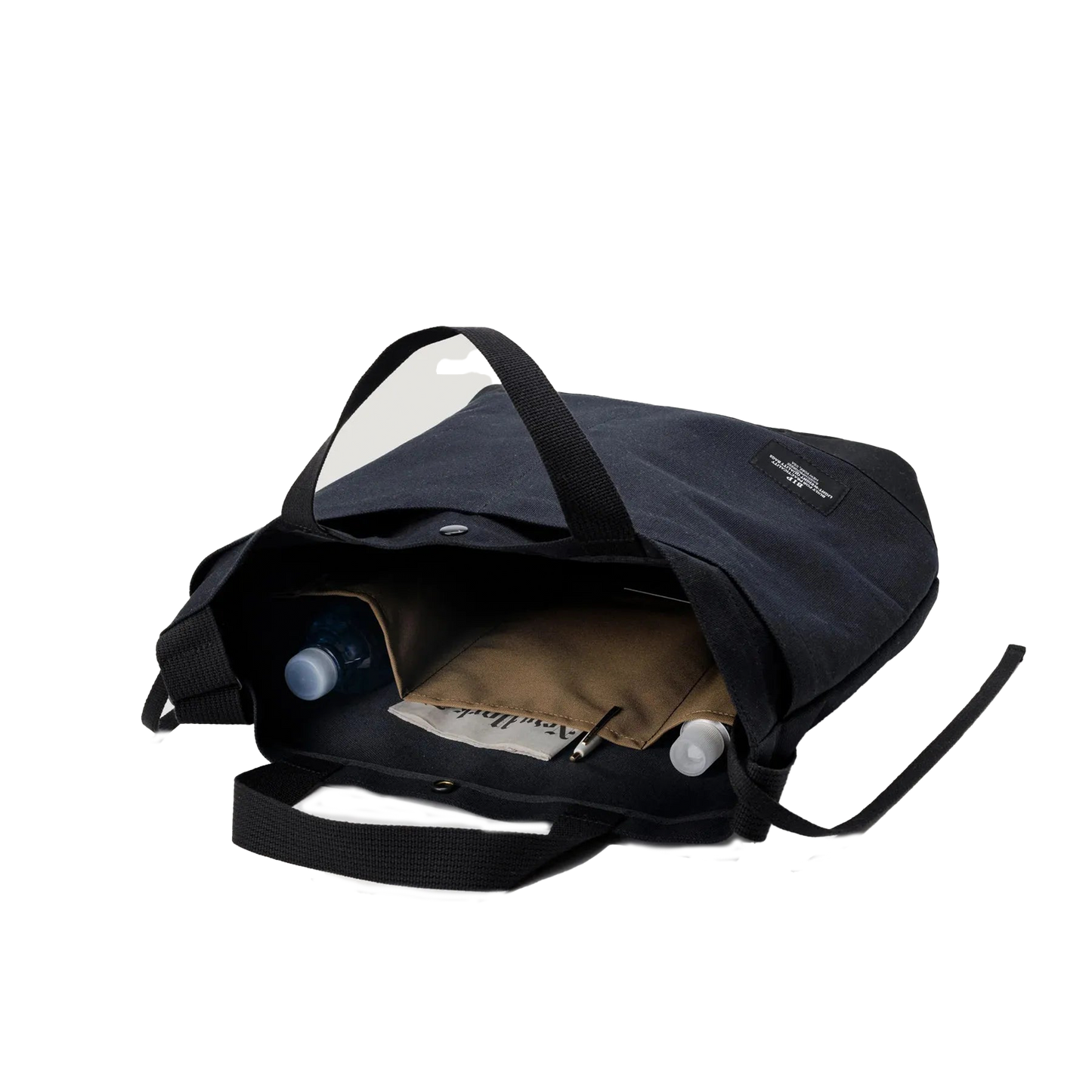 The Bags in Progress New York Tote Medium, an open black cotton canvas bag with an adjustable shoulder strap, displays a water bottle, folder, and notebook in its compartments against a plain background.