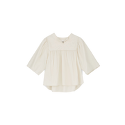 The Nomi Blouse by Aiayu features a cream color with long sleeves, a pleated front, and a wide collar, all crafted from sustainable materials. This 70s-inspired design is elegantly captured against a plain black background.