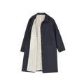 The Noor Coat Oil by Aiayu is a classic black overcoat with buttons and a white lining, shown open to display the label. Made from wax-coated organic cotton, it combines style with excellent weather protection.