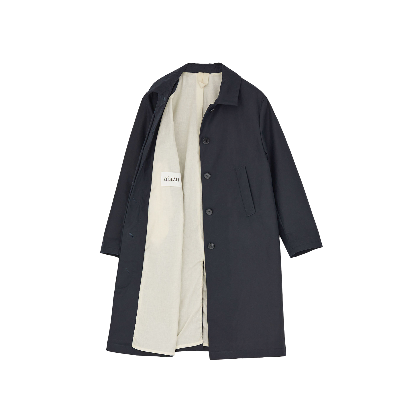 The Noor Coat Oil by Aiayu is a classic black overcoat with buttons and a white lining, shown open to display the label. Made from wax-coated organic cotton, it combines style with excellent weather protection.