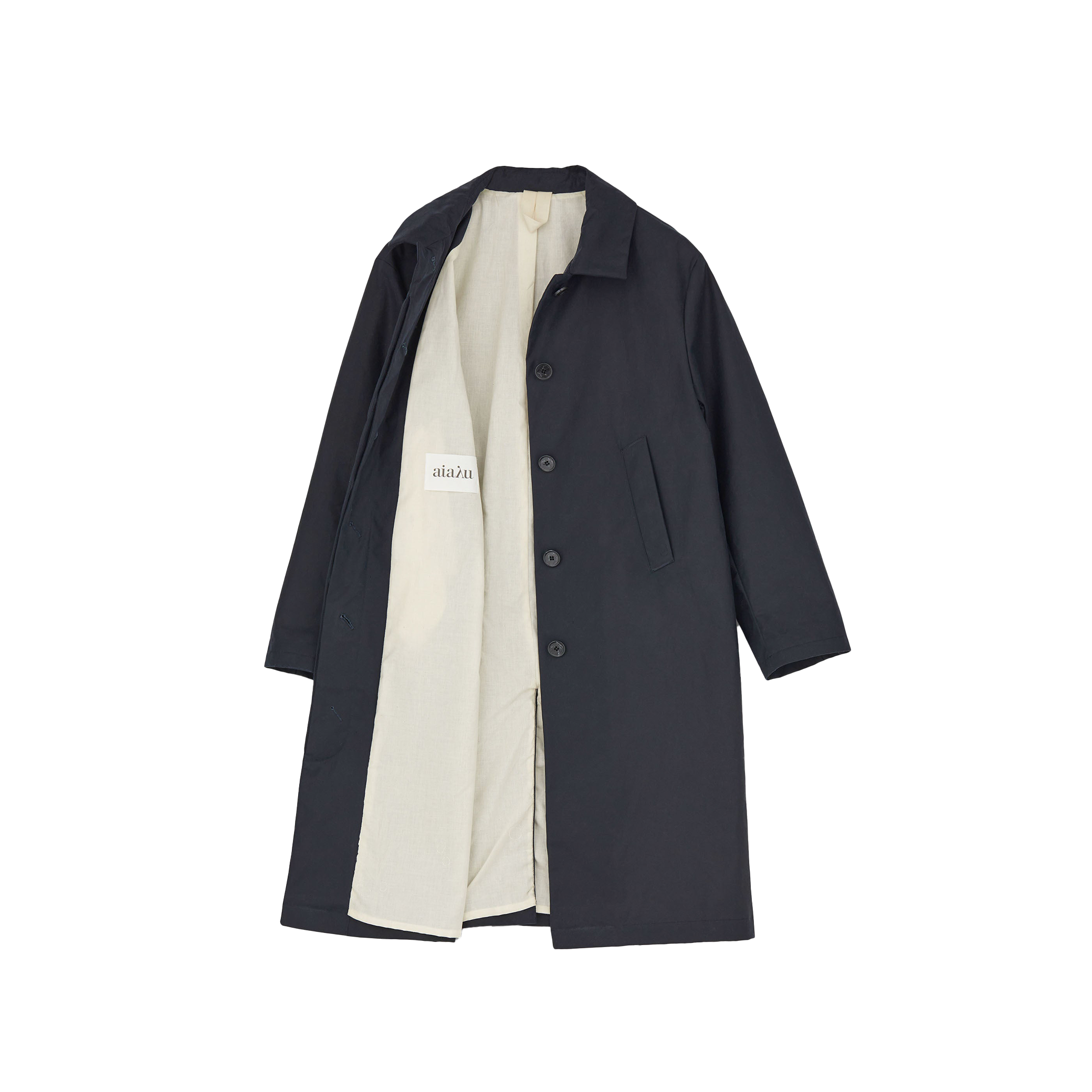 The Noor Coat Oil by Aiayu is a classic black overcoat with buttons and a white lining, shown open to display the label. Made from wax-coated organic cotton, it combines style with excellent weather protection.