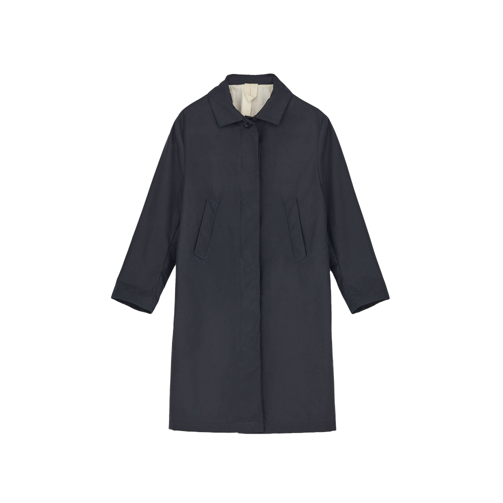 The Noor Coat Oil by Aiayu is a long, dark classic coat made from wax-coated organic cotton, featuring a classic collar and two front pockets, displayed on a plain background.